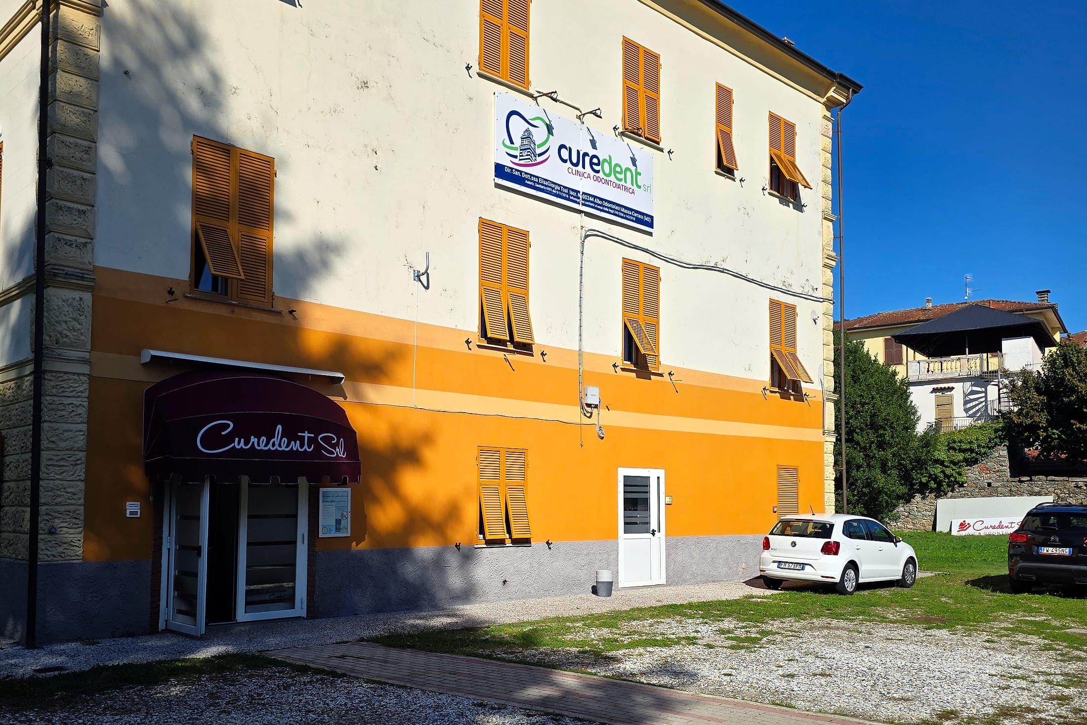La facciata di Curedent in Via Roma 8, con l'insegna e la tenda bordeaux sull'ingresso